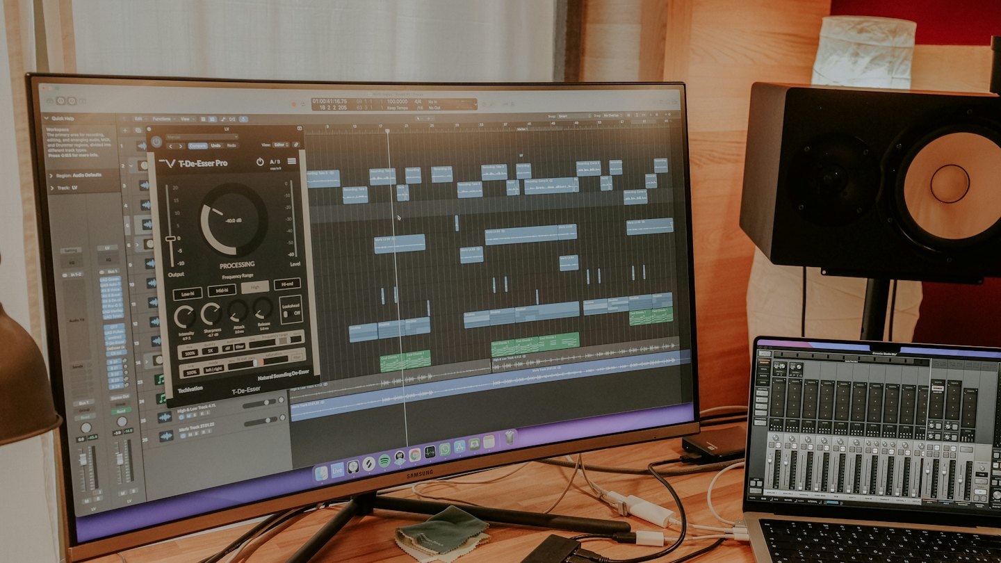Estación de trabajo de producción musical con software de edición de audio en un monitor curvo.