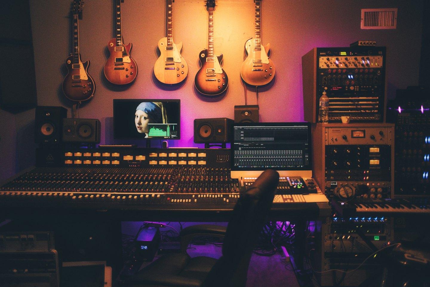 Consola de mezclas y guitarras en un estudio de grabación con iluminación púrpura.