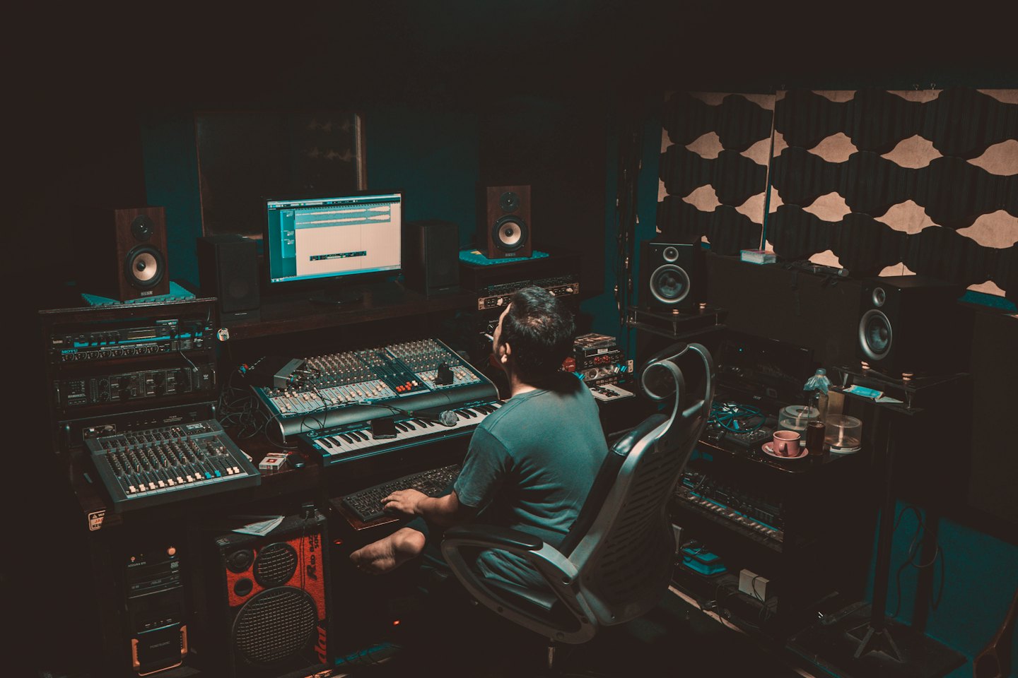 Hombre trabajando en una mesa de mezclas de sonido y monitores de computadora.